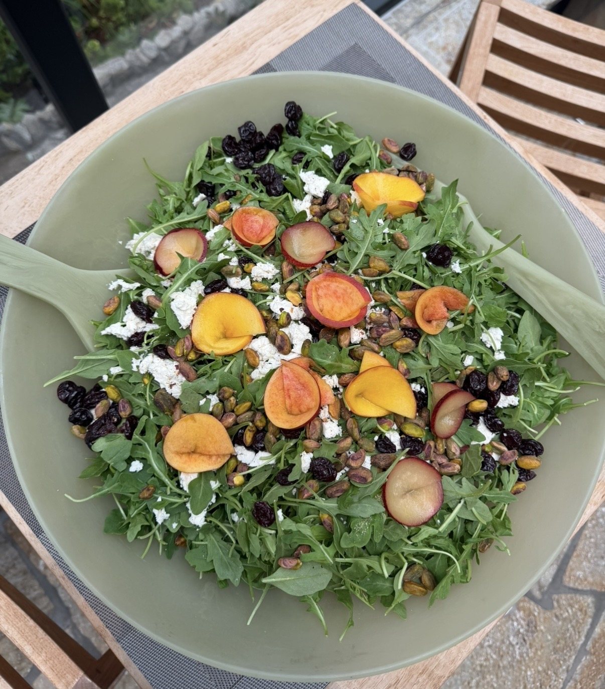 Arugula salad with stone fruit, cheese, and pistachios in a green bowl