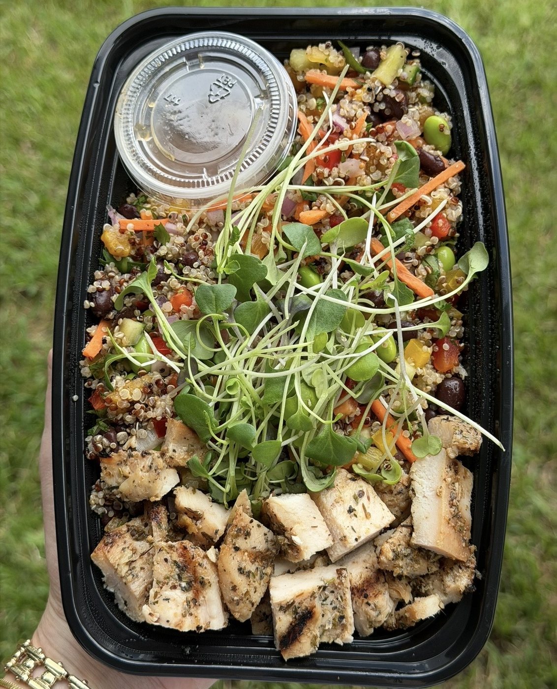 A meal-prep container of grilled chicken, quinoa salad, and dressing