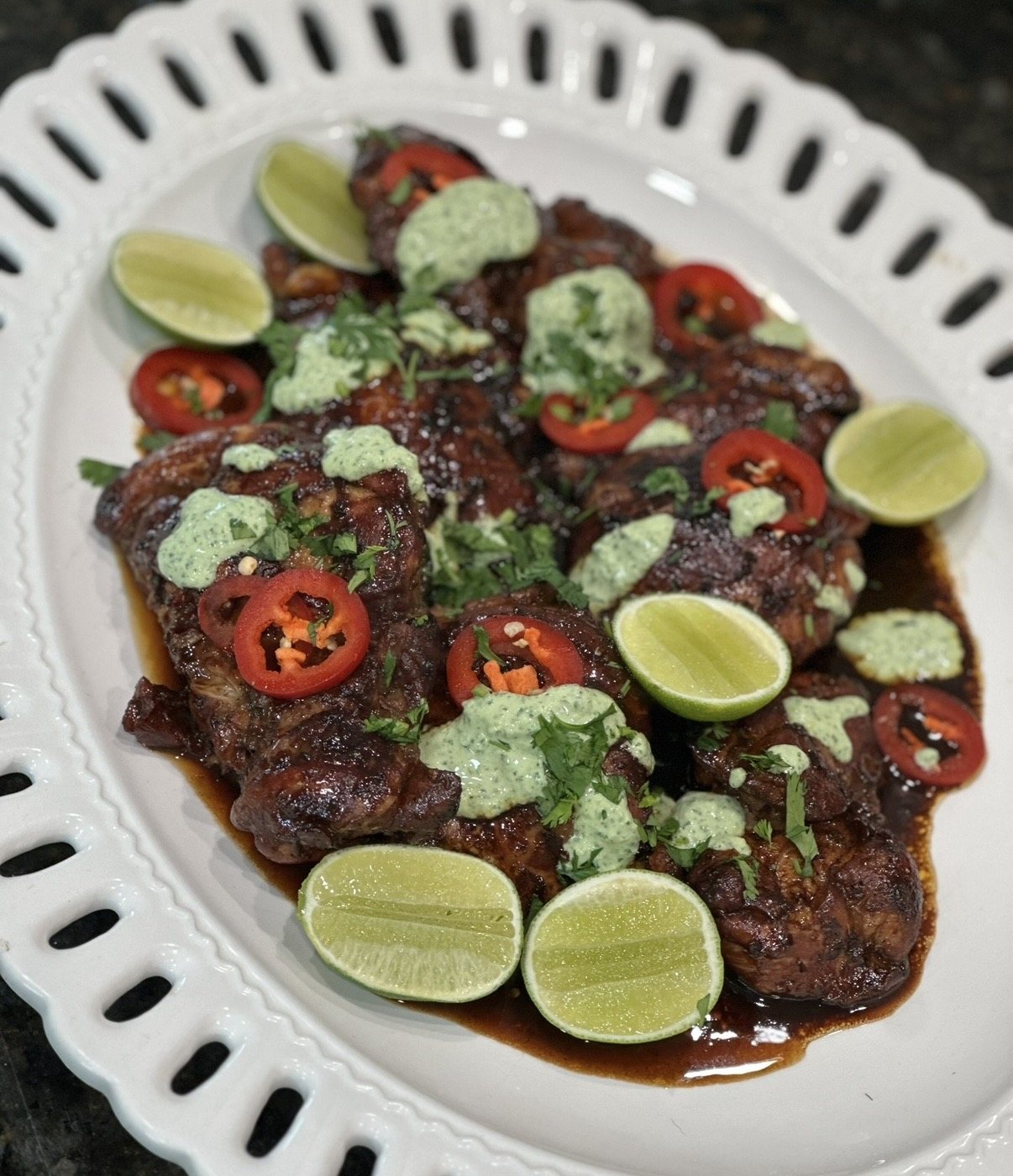 Glazed chicken on a scalloped platter with herbs, chili, and lime