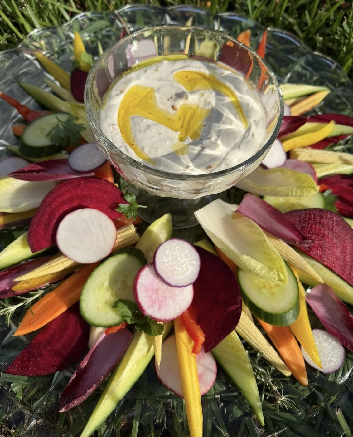 A colorful crudité platter of sliced vegetables around a bowl of dip