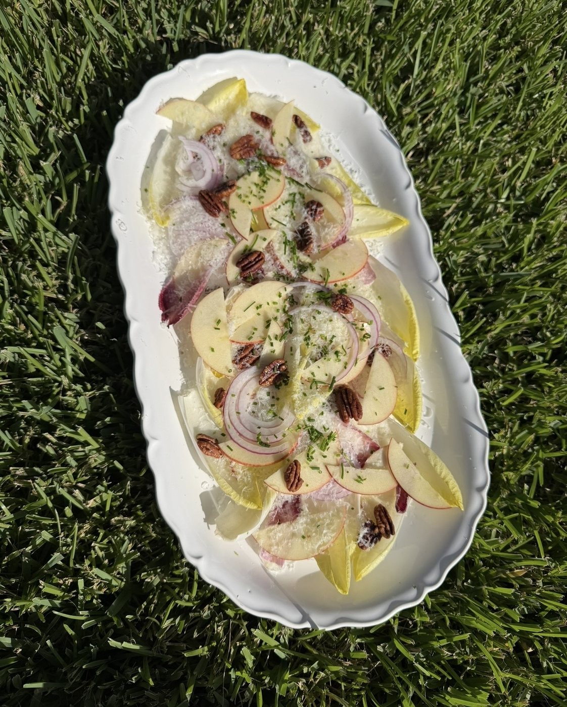 Endive and apple salad with pecans and grated cheese on an oval platter