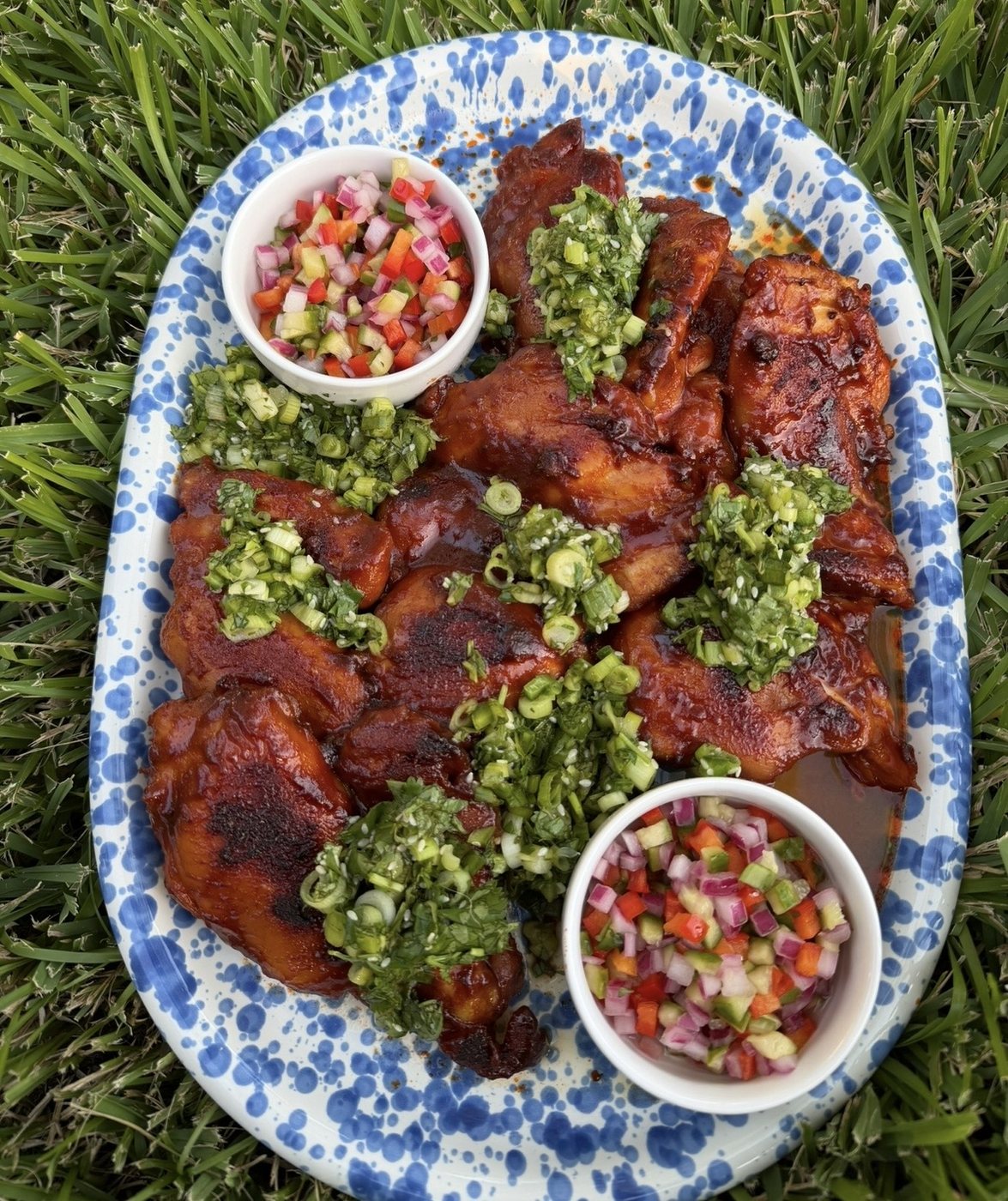 Glazed grilled chicken on a blue-and-white platter with herb topping and salsa