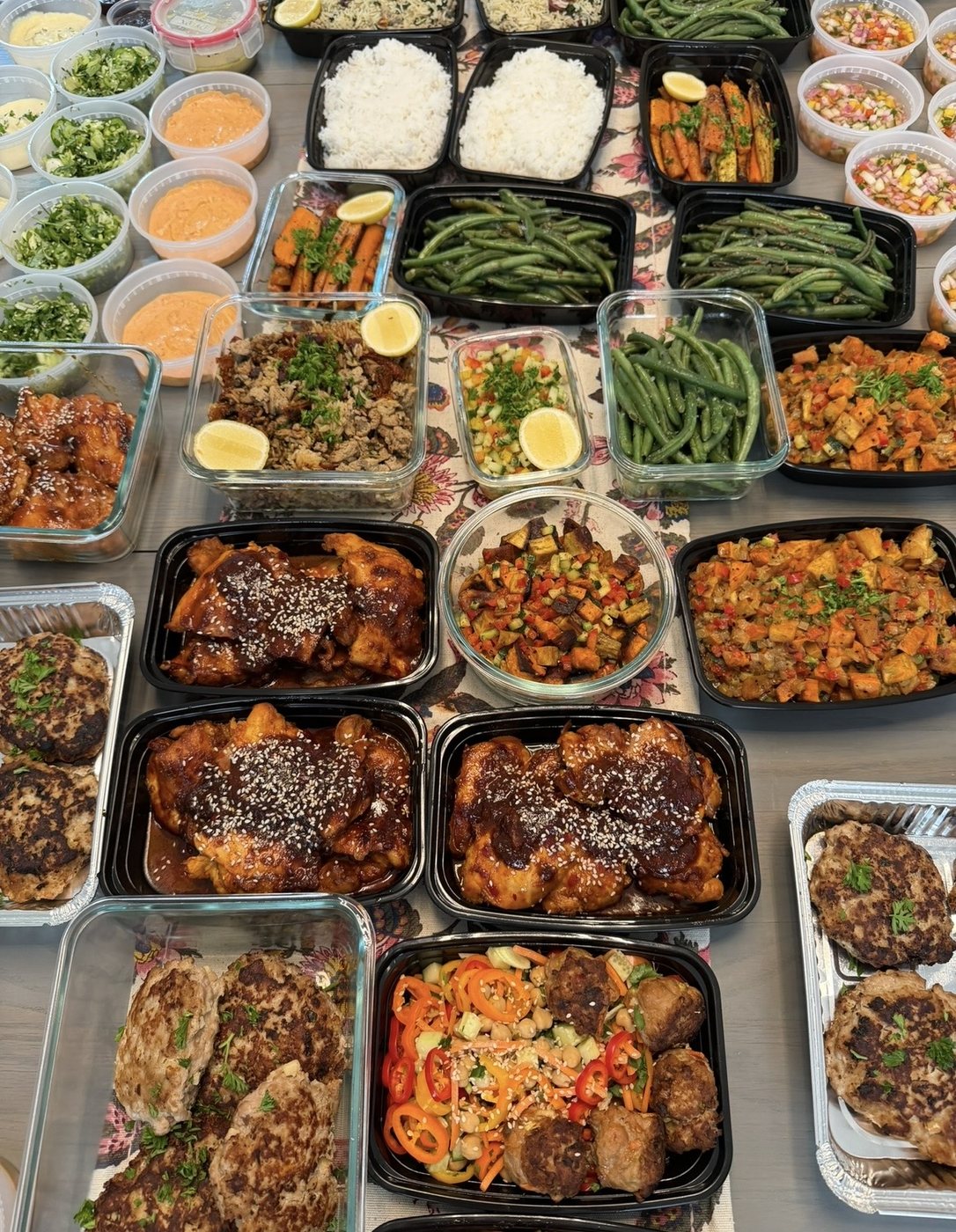 A table of weekly meal-prep containers with chicken, vegetables, rice, and sauces